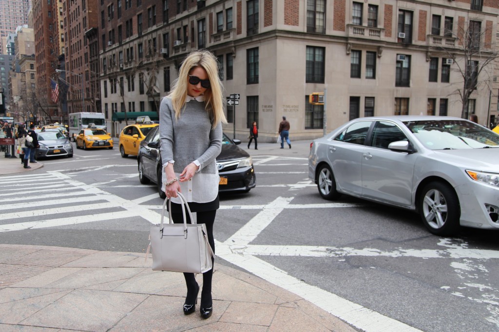 Caitlin Hartley of Styled American in a layered sweaterholding a grey tote