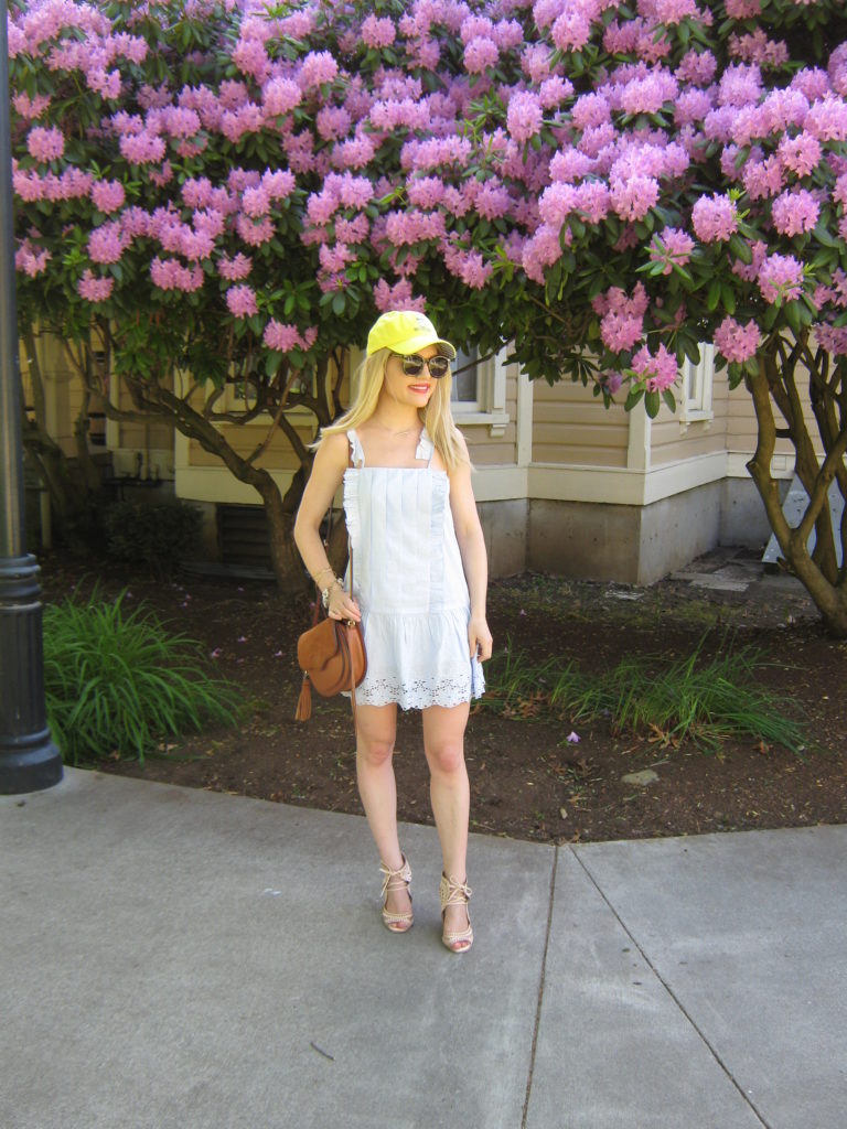 Caitlin-Hartley-of-Styled-American-in-front-of-purple-flowers-blue-dress-and-baseball-cap