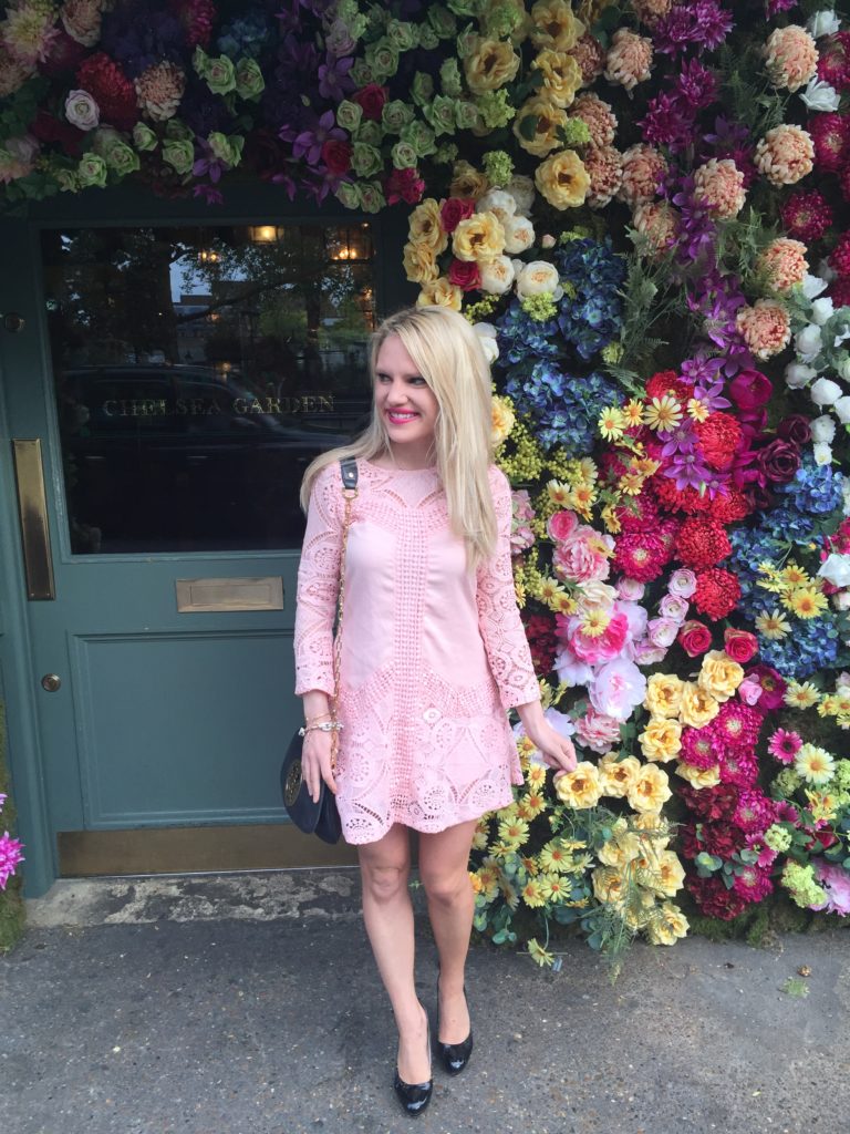 Caitlin-of-Styled-American-pink-lace-dress-black-bag-black-pumps-in-front-of-ivy-flower-wall